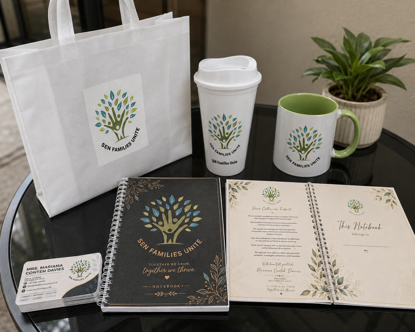 SEN Families Unite branded bag, mug, travel cup, notebook and business cards displayed on a table.