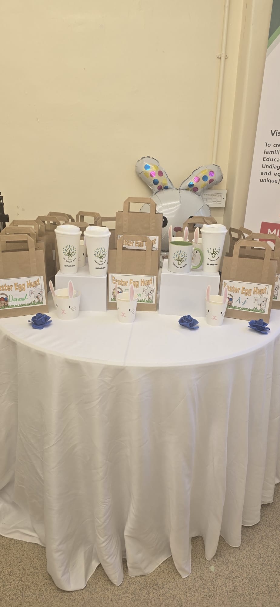 Easter Egg Hunt display with gift bags, SEN Families Unite mugs and travel cups on a decorated table.